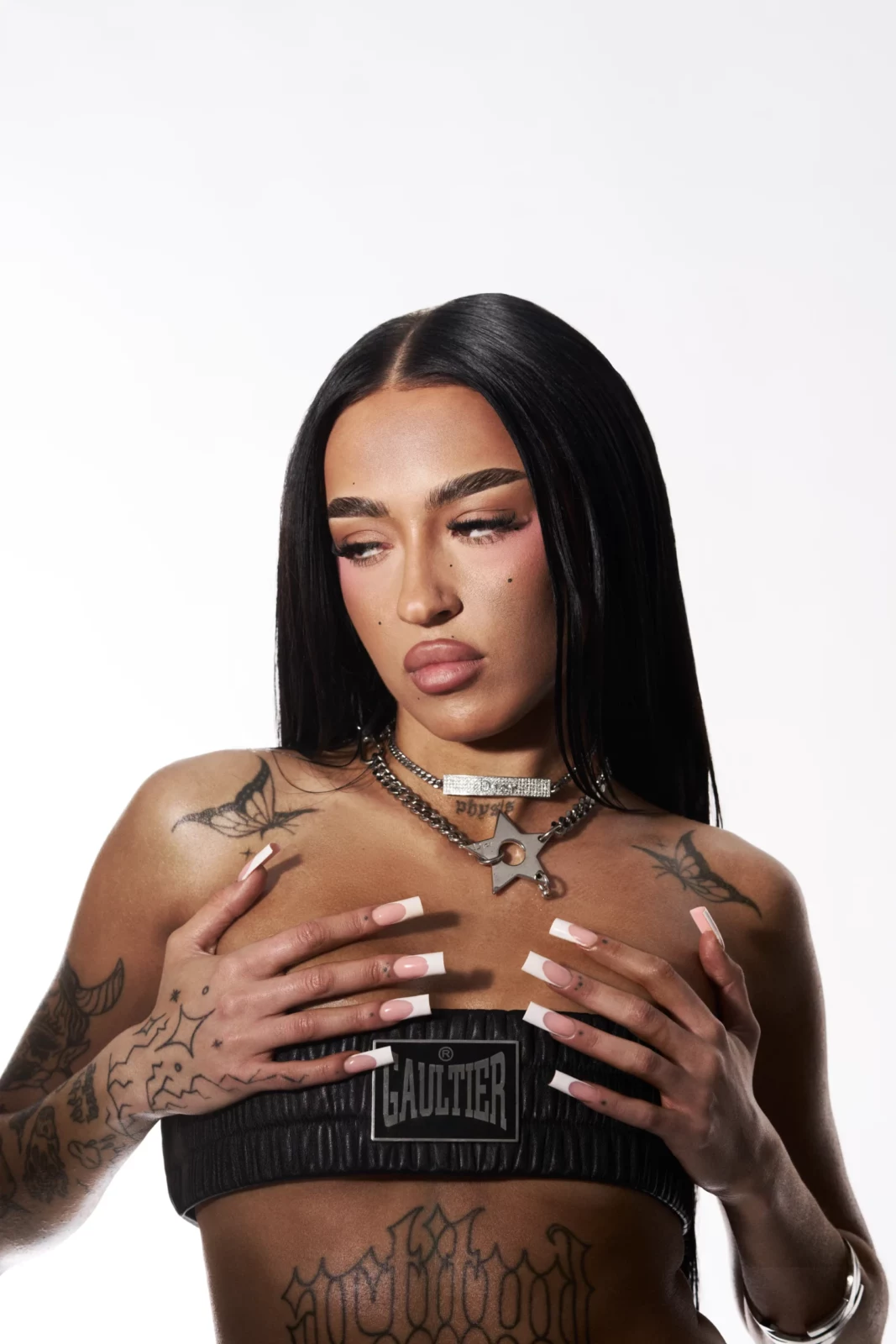 Close-up portrait of a woman with long black hair and metallic body jewelry in a white studio.