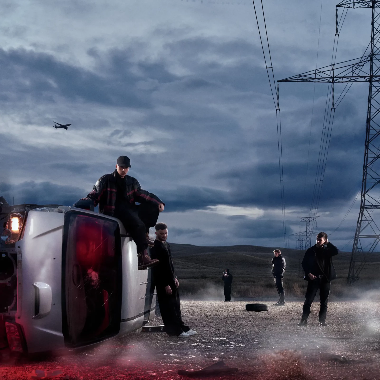 Moody dusk album-cover photograph of a person perched on an overturned vehicle beside an empty roadway.