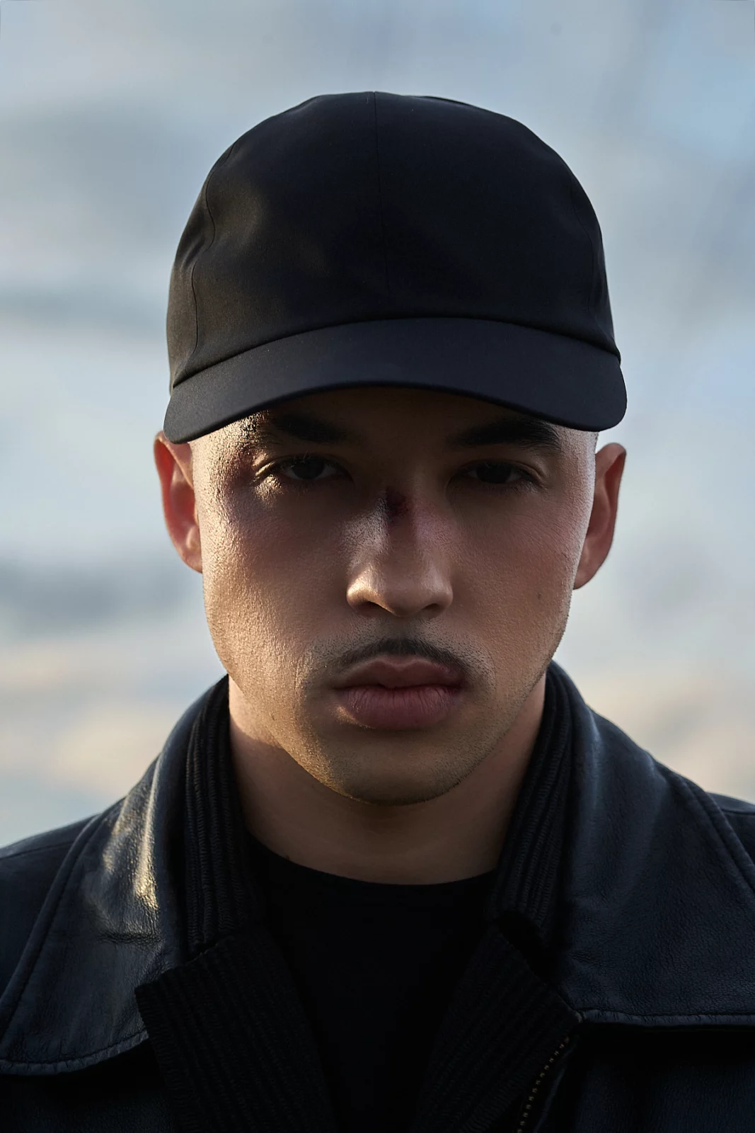 Close-up portrait of Pole wearing a black baseball cap and dark jacket under an overcast sky.