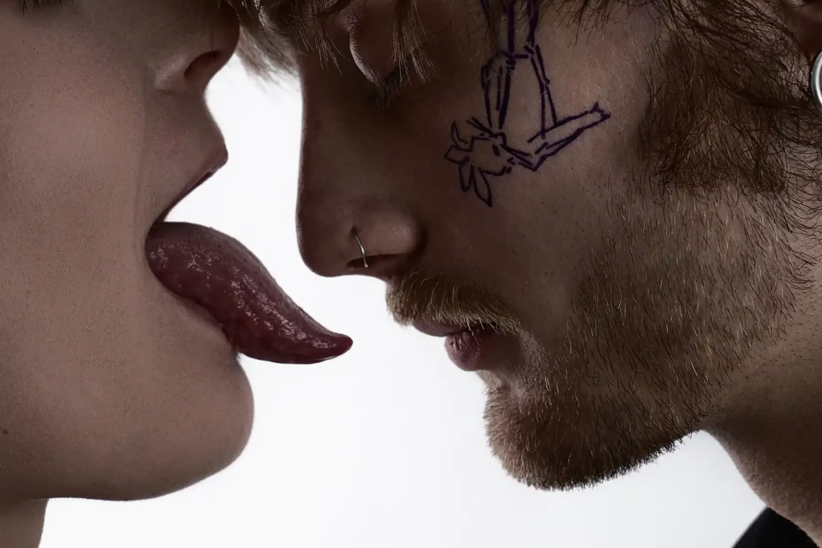 Extreme close-up of a tongue reaching toward a man's face with a purple line-art tattoo design.