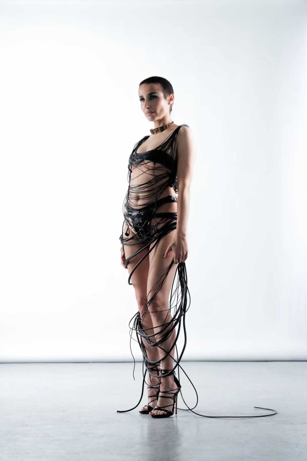 Full-length portrait of Zahara in a black strappy outfit with long cords trailing across the white studio floor.