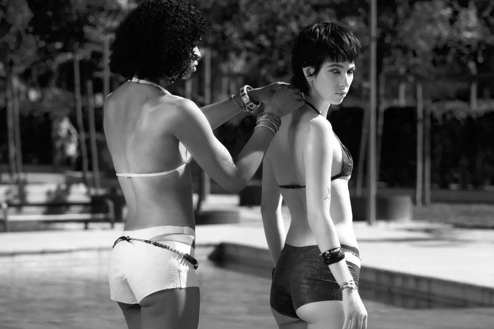 Black-and-white photograph of two women in bikinis standing by a sunlit fountain.