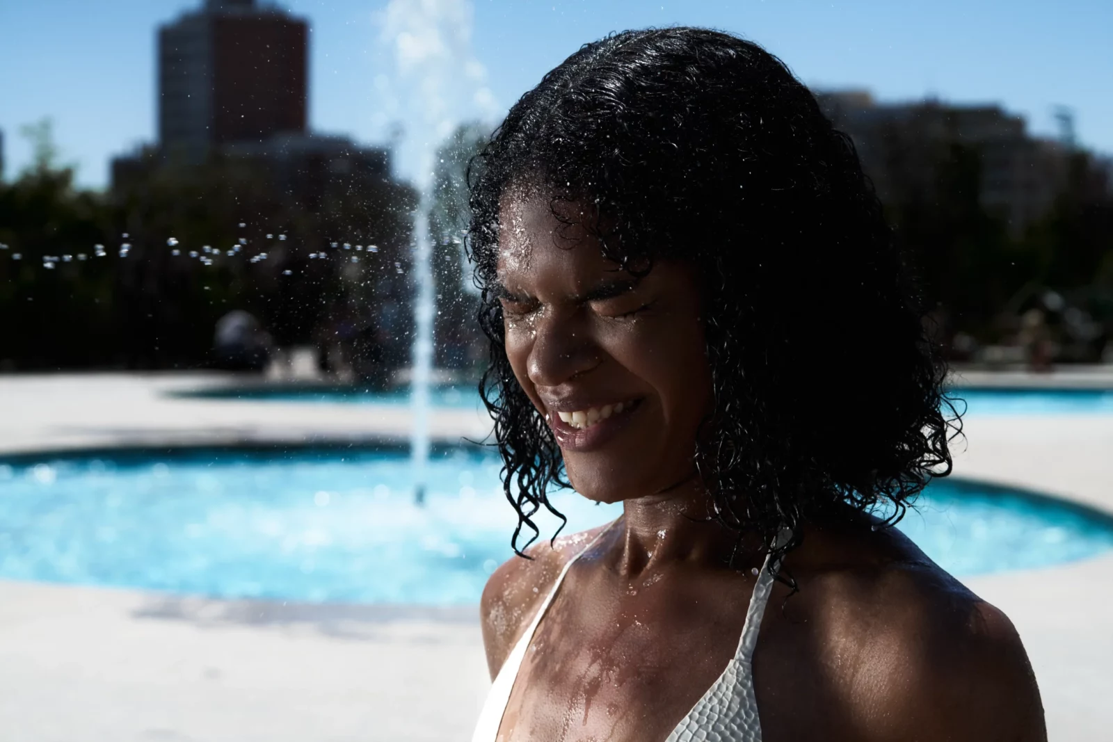 Close-up portrait of a smiling curly-haired woman in a white bikini with water droplets on her skin.