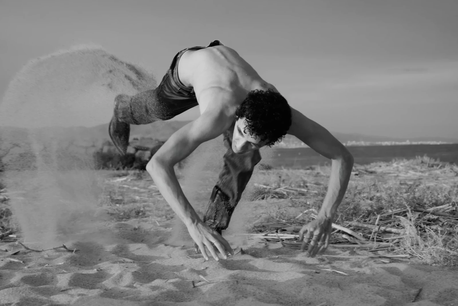Black-and-white photograph of a shirtless model crawling on all fours through dust and dry earth.