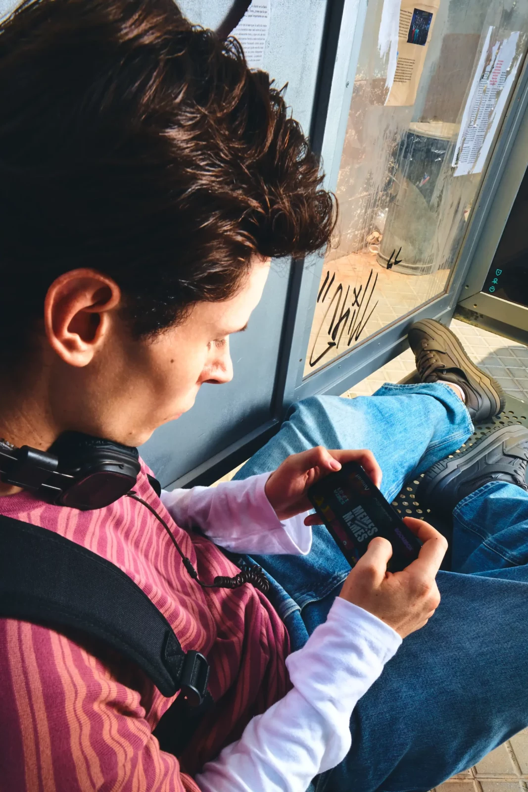 Side profile of a young man looking down at a compact blue device on a city street.