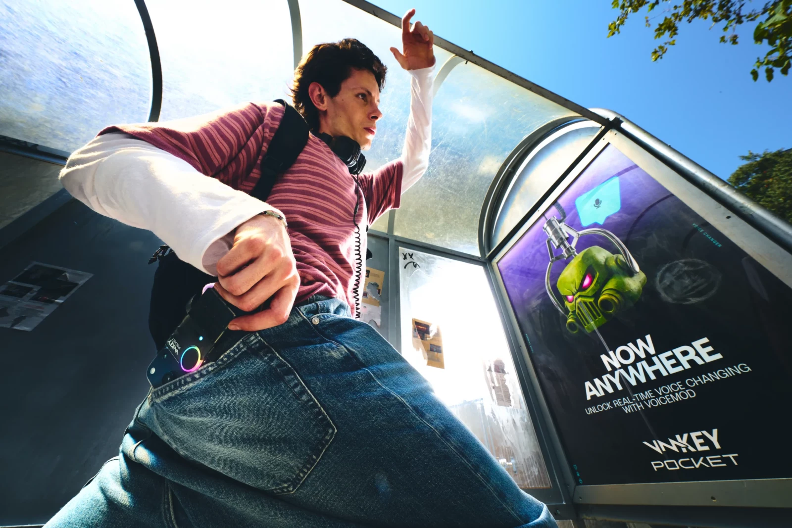 Low-angle streetwear portrait of a man with a blue audio device beside an open car door under a bright sky.