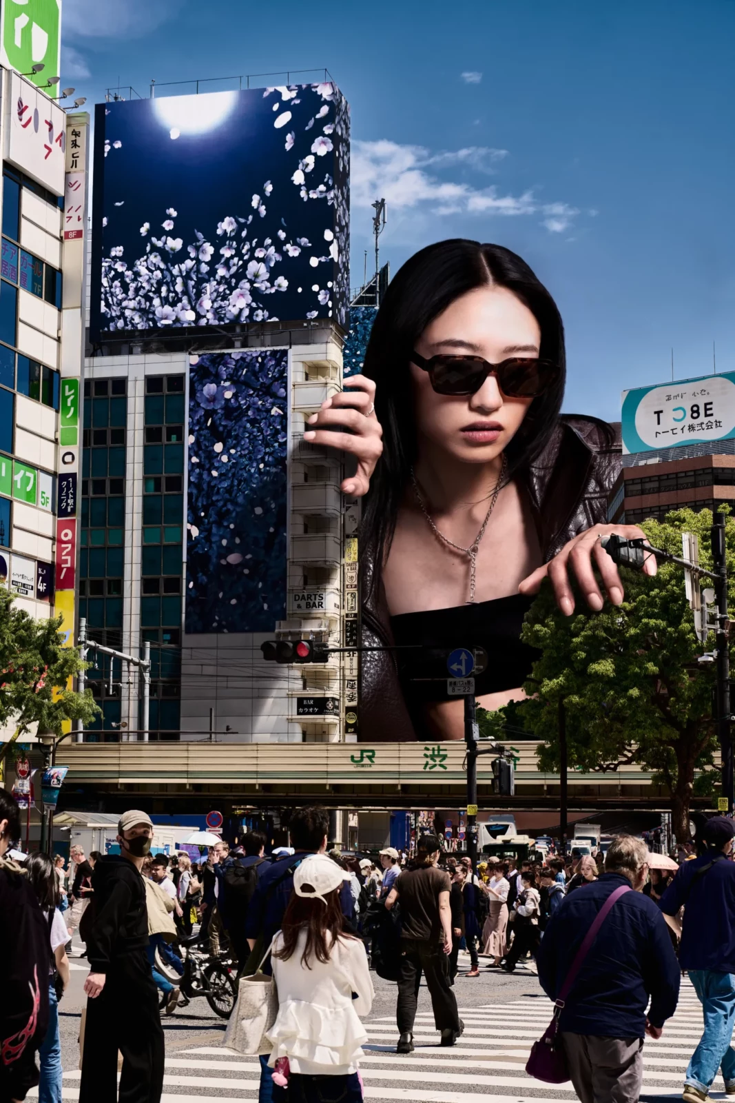 Tall urban billboard featuring a sunglasses portrait above a crowded Japanese pedestrian crossing.