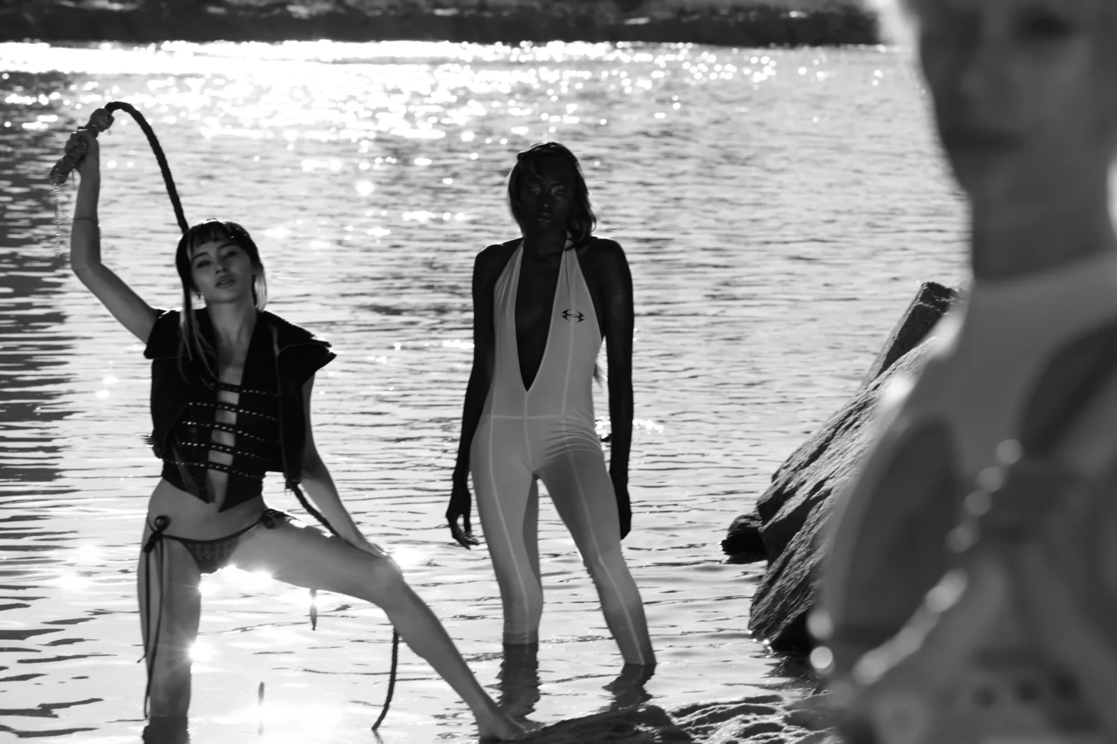 Black-and-white fashion group photographed by the water, with two models holding long objects.
