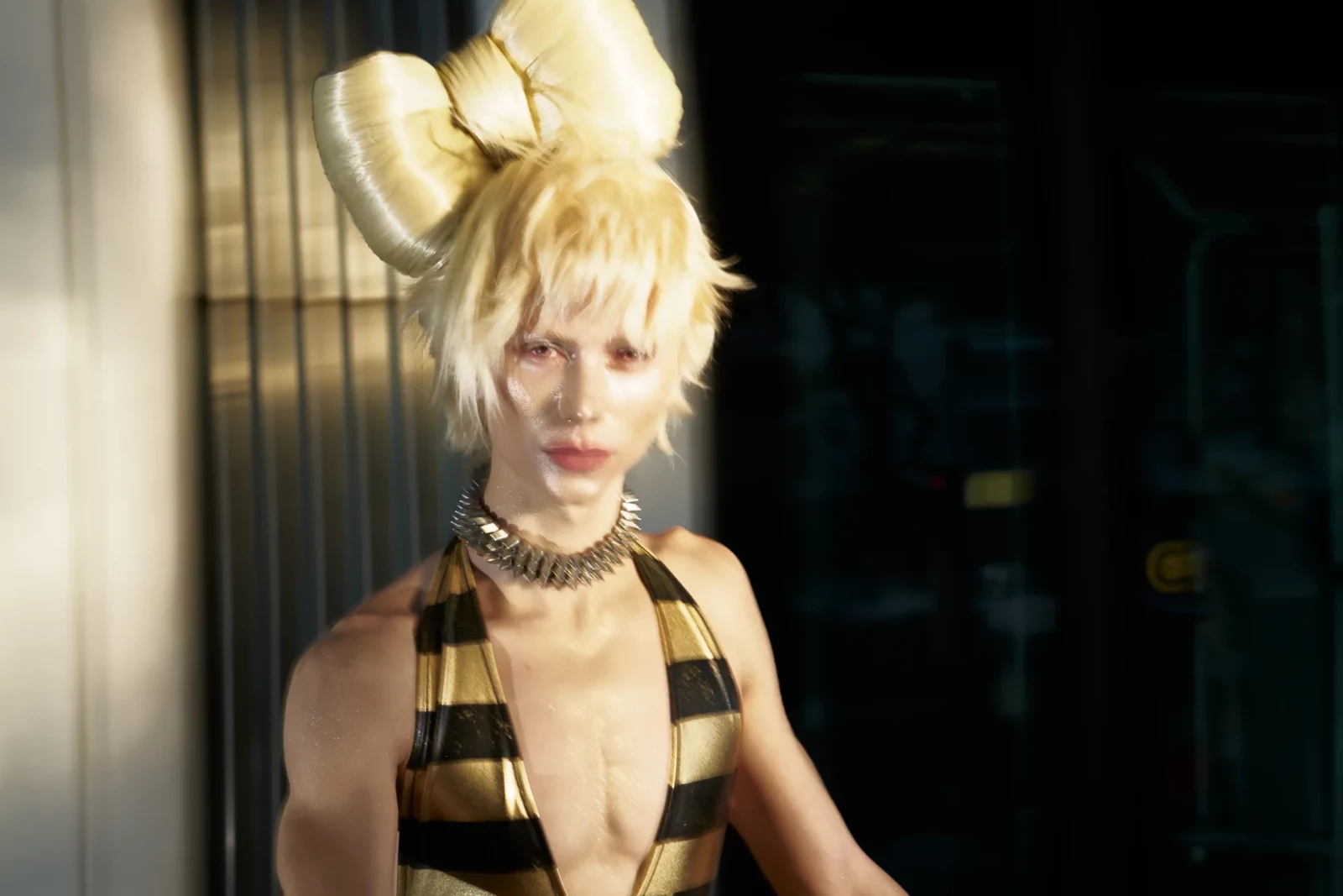 Close-up portrait of a blonde model in a striped halter outfit and dramatic sculptural hairstyle.