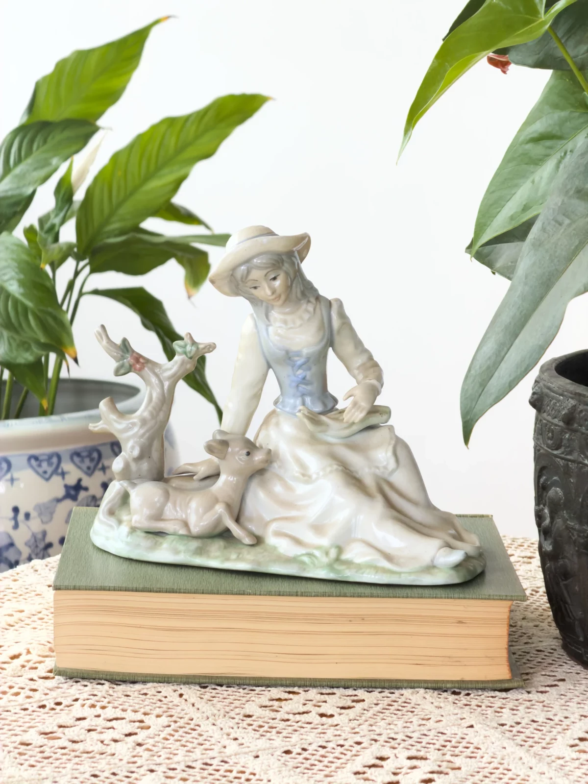 White porcelain figurine of two people surrounded by green houseplants in a bright room.