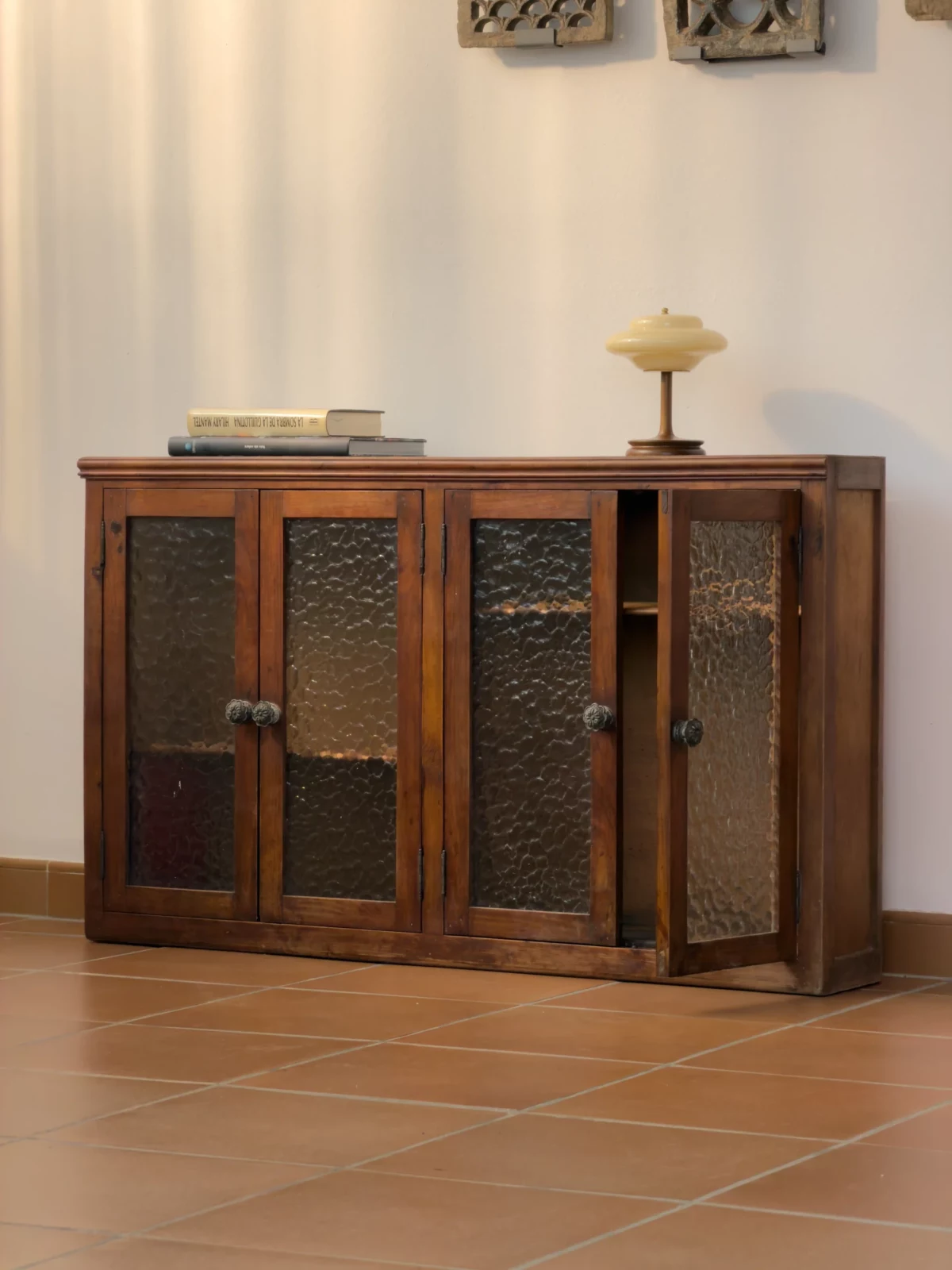 Dark wooden cabinet with glass-panel doors against a pale wall, with small decorative objects on top.