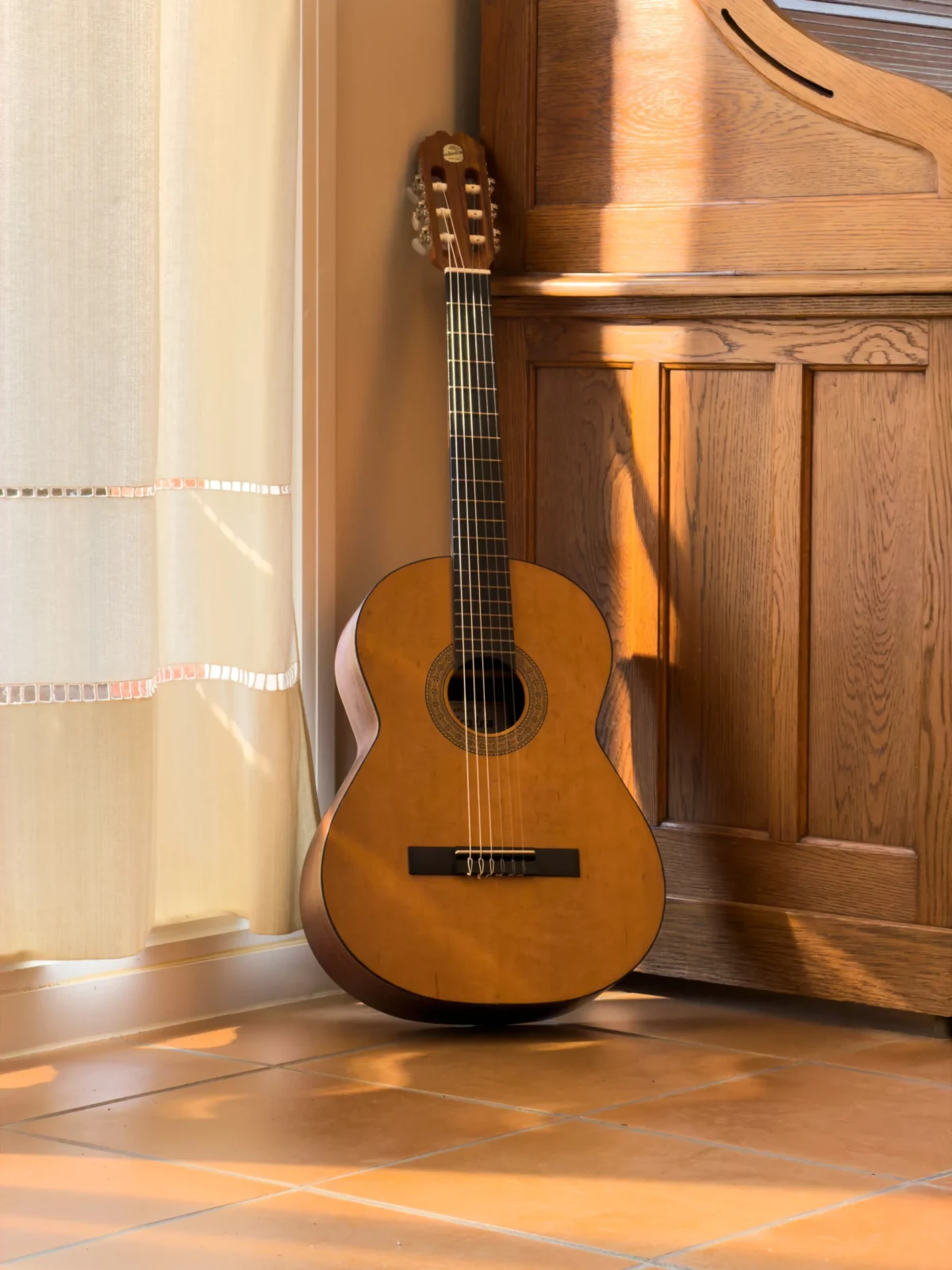 Acoustic guitar leaning against a wooden cabinet on warm parquet flooring.