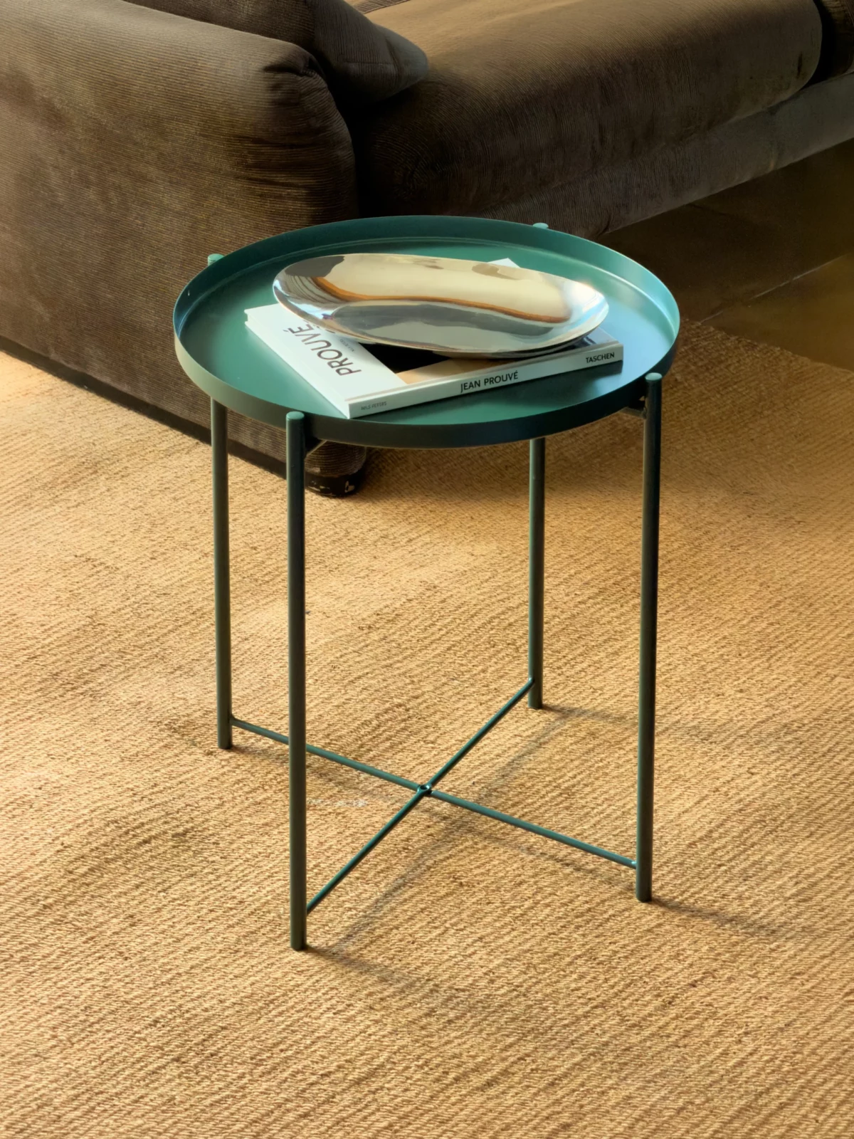 Small round green side table holding a pale dish on a cream rug beside a sofa.