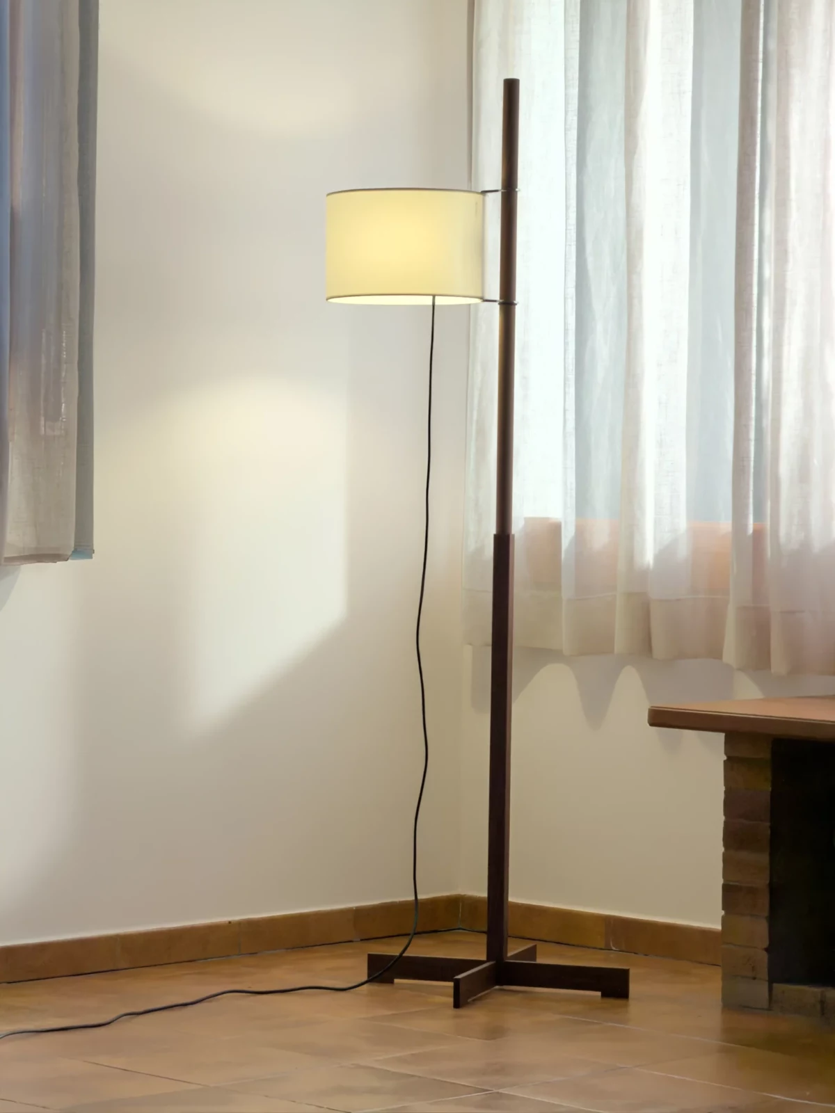Slender floor lamp with a cream shade standing by sheer curtains in a minimal living room.