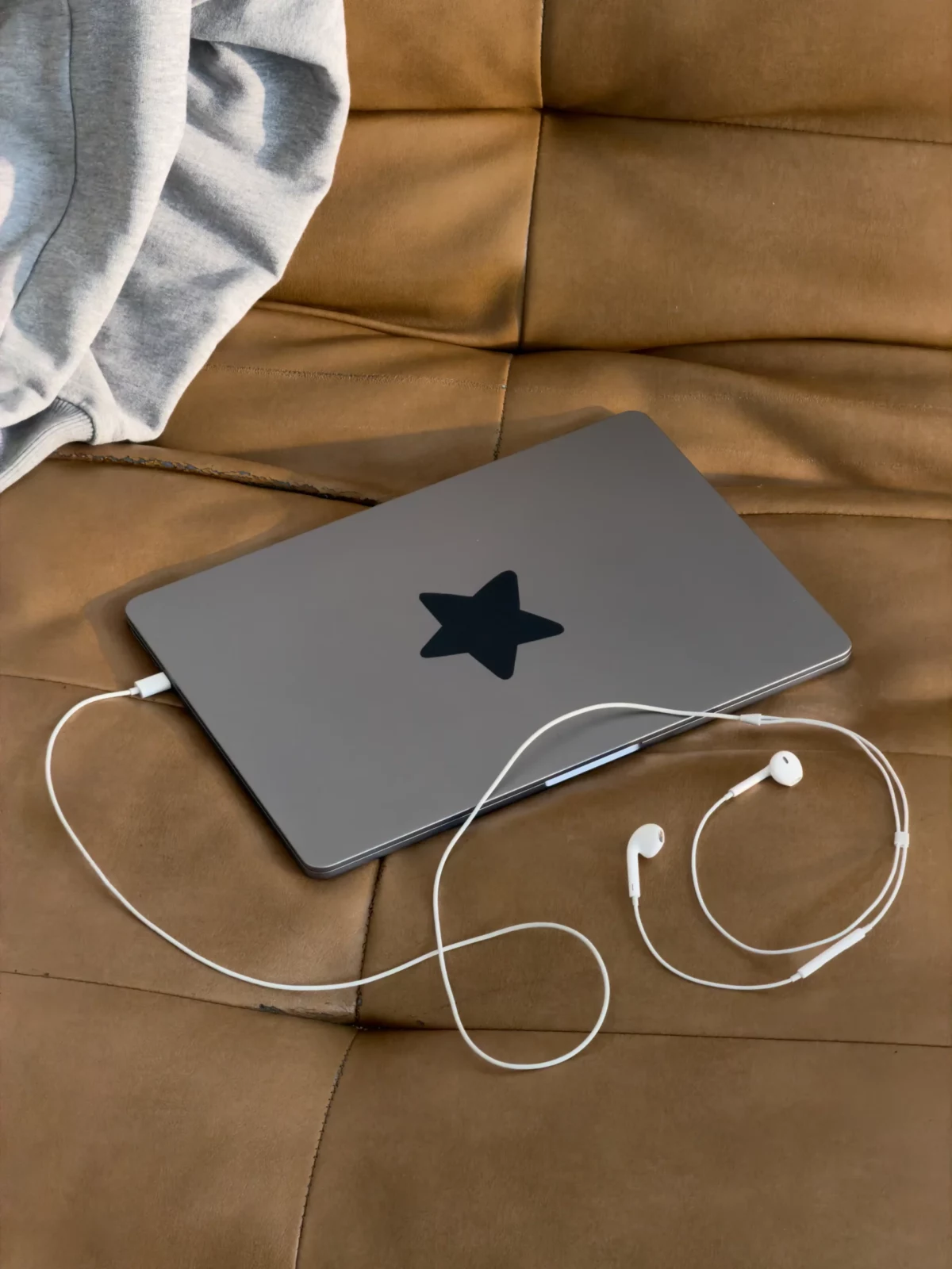 Gray electronic tablet with a star sticker and wired earbuds resting on a tan leather sofa.