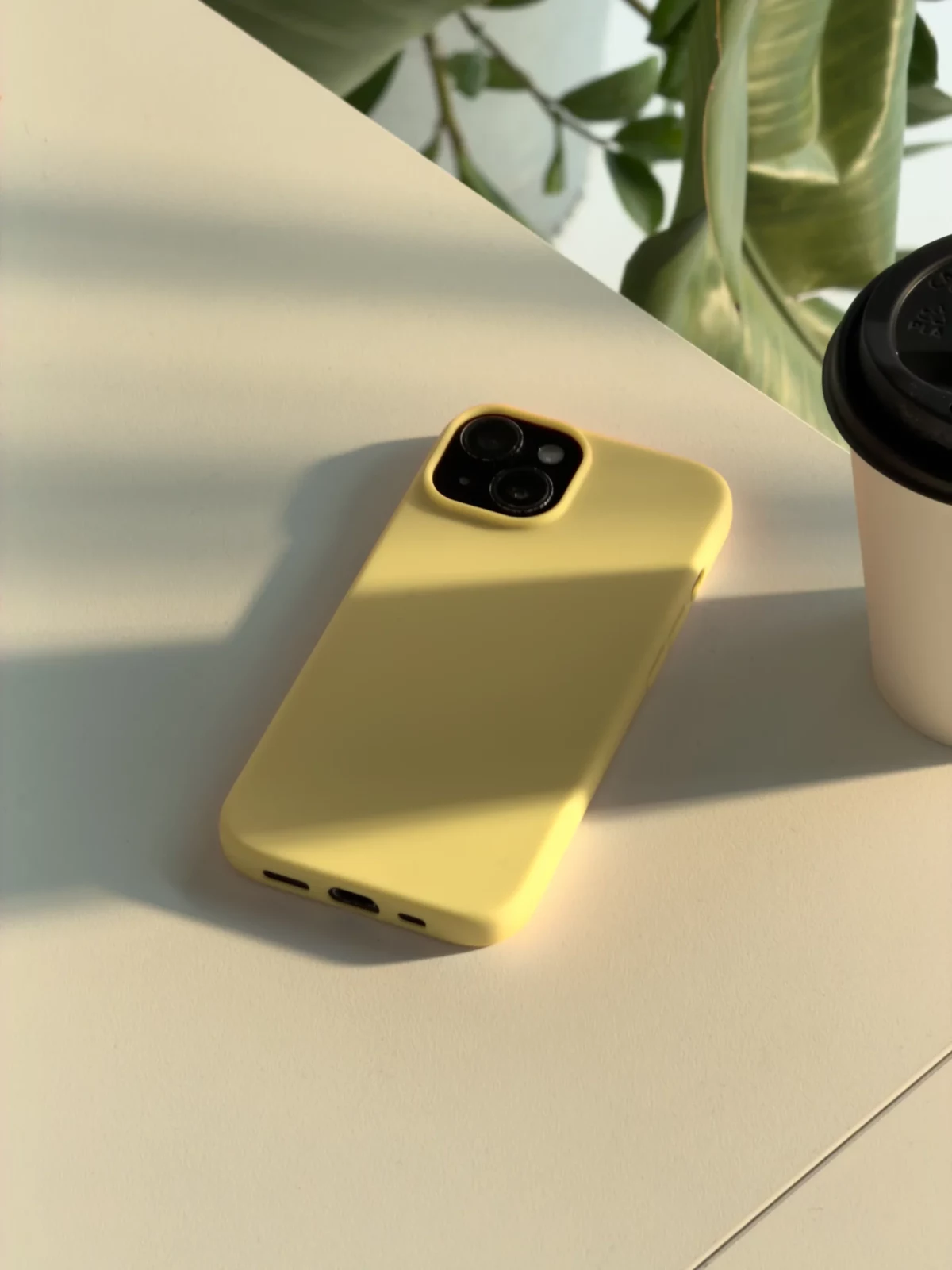Yellow smartphone standing upright on a pale table beside an indoor plant.