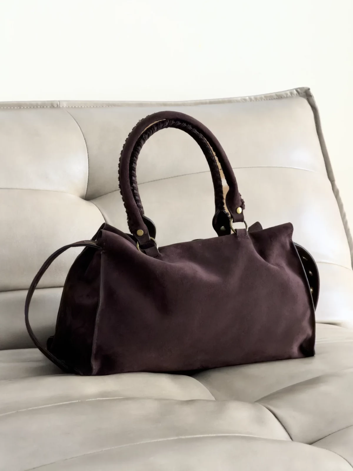 Dark brown leather handbag with curved handles placed on a cream leather sofa.