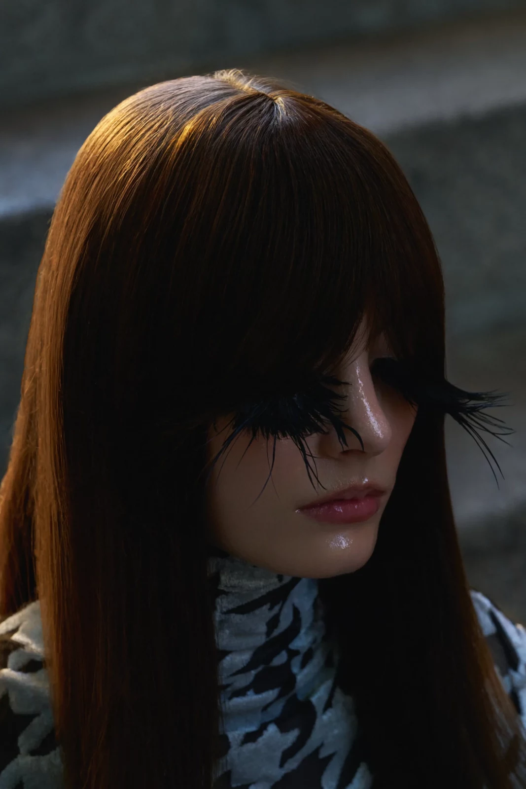 Side portrait of a dark-haired model with a straight fringe wearing a patterned high-neck top.