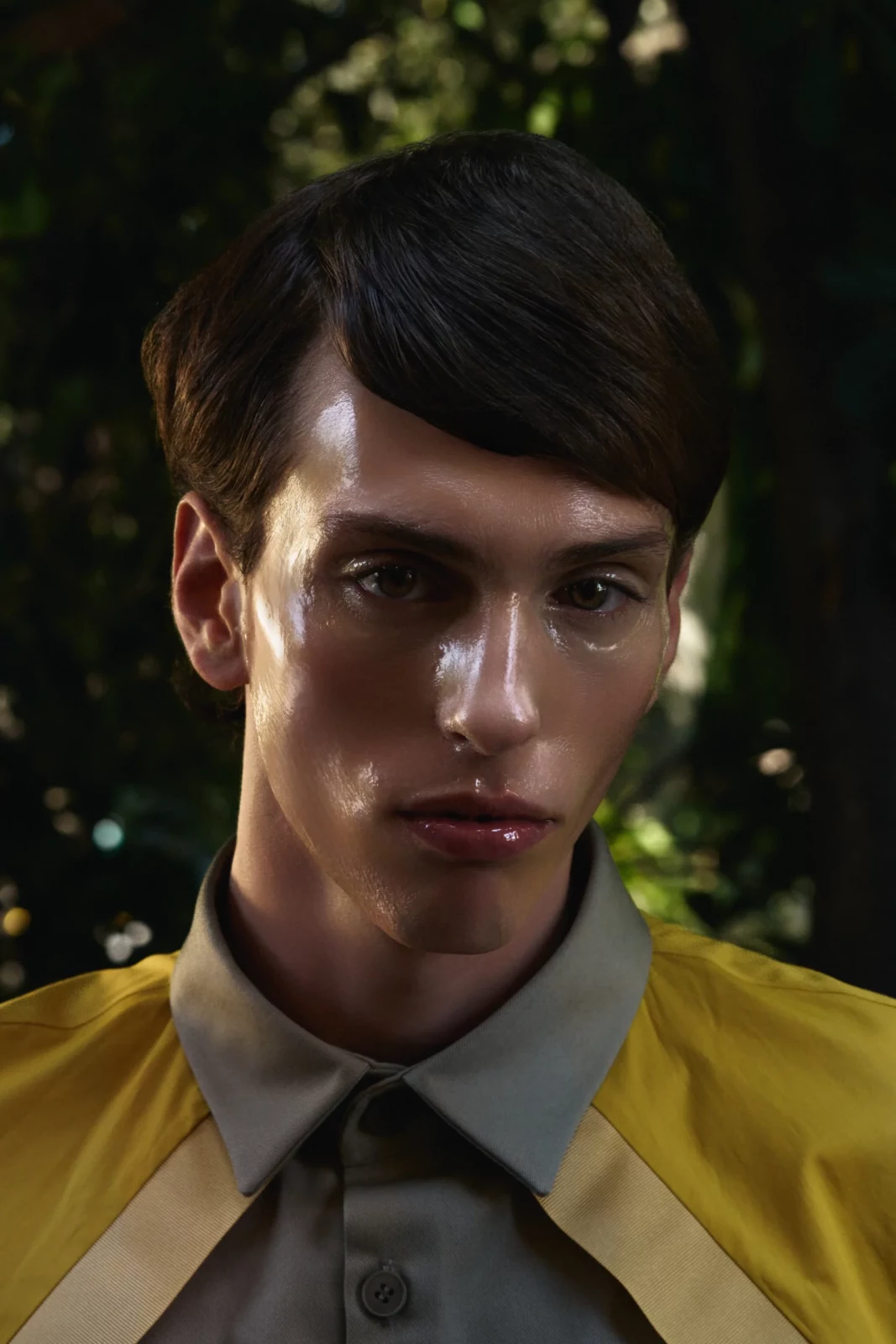 Close-up portrait of a male model in a bright yellow jacket and tie in a leafy courtyard.