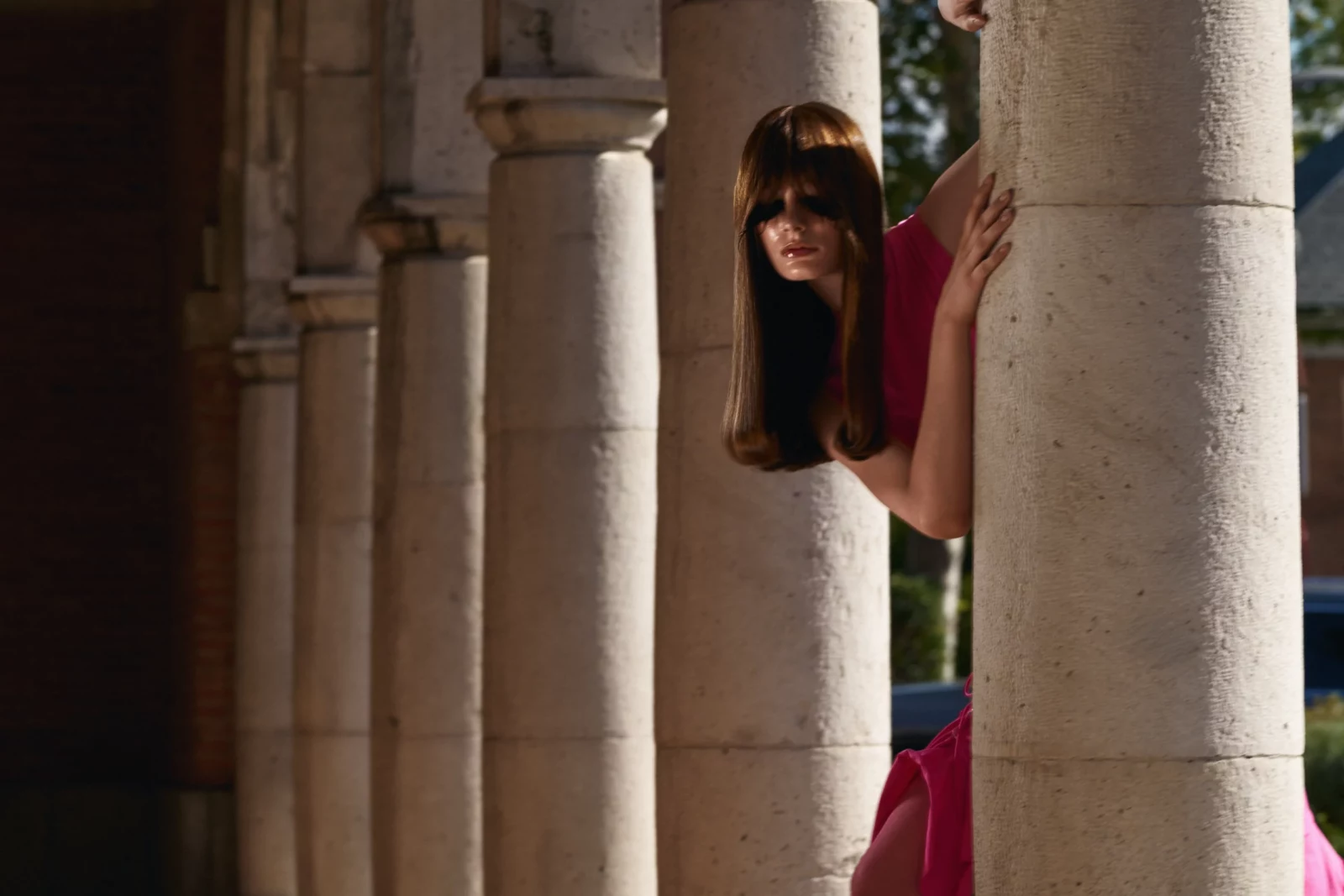 Fashion model wearing pink clothing peering around a row of stone columns.