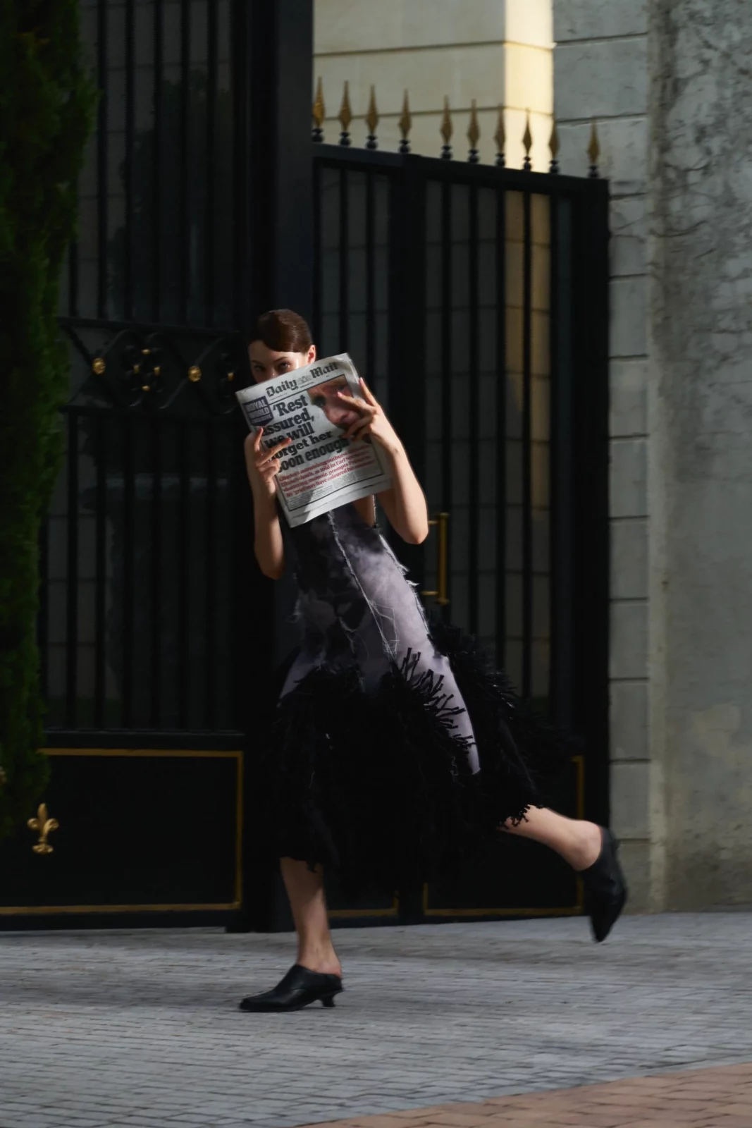 Model in a dark skirt and striped shirt running past a tall wrought-iron gate.
