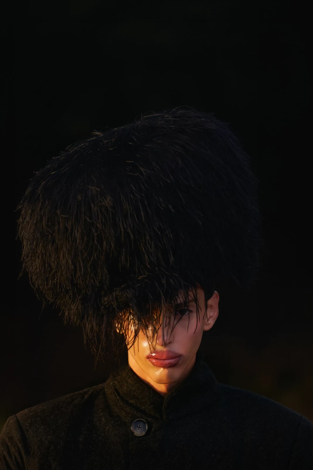 Low-key portrait of a male model with dark hair covering his eyes against a black background.