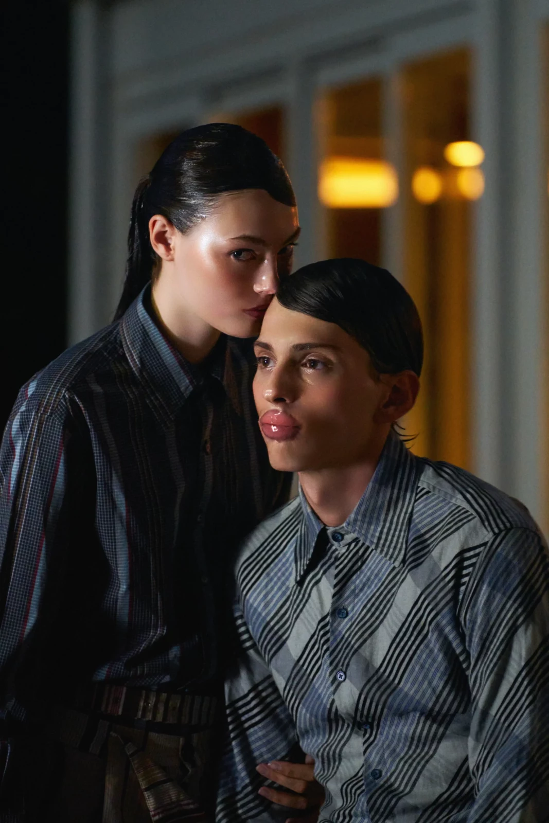 Intimate portrait of two fashion models in blue-gray shirts standing together under warm evening light.