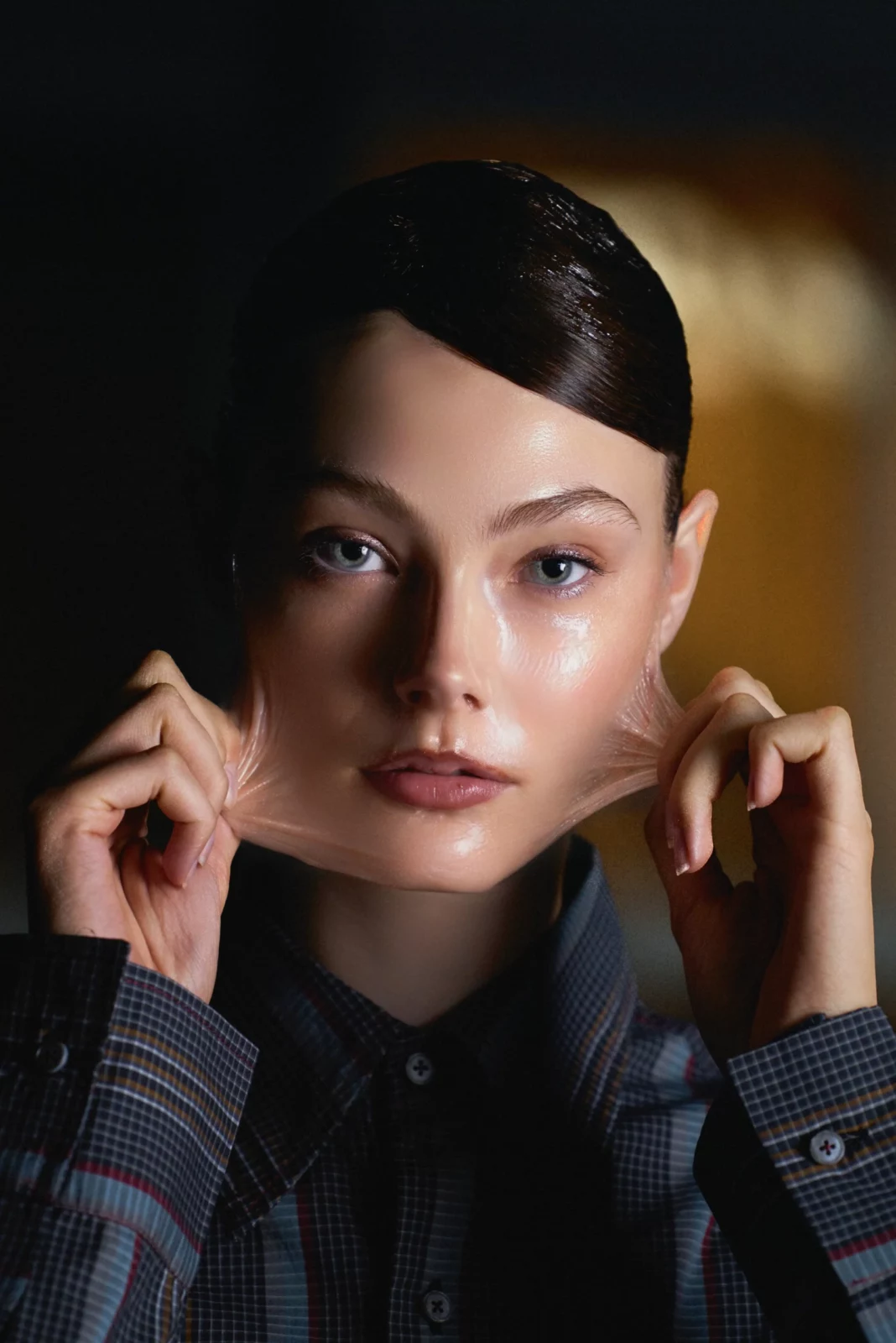 Close-up beauty portrait of a dark-haired model in a tailored jacket with both hands framing the face.