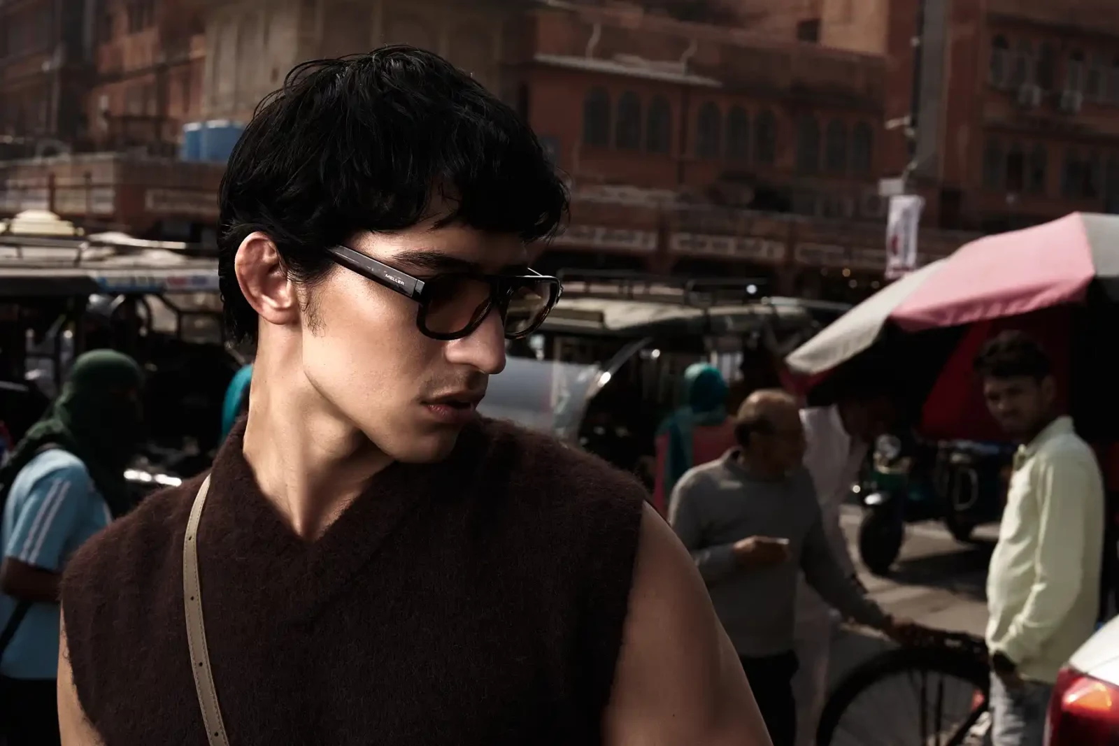 Side-profile portrait of a short-haired man in black sunglasses and a dark sleeveless top outdoors.