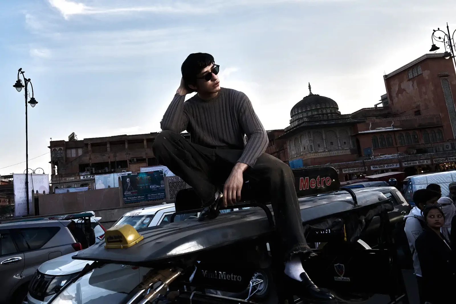Man in sunglasses and a dark shirt posing beside a classic car on a city street.