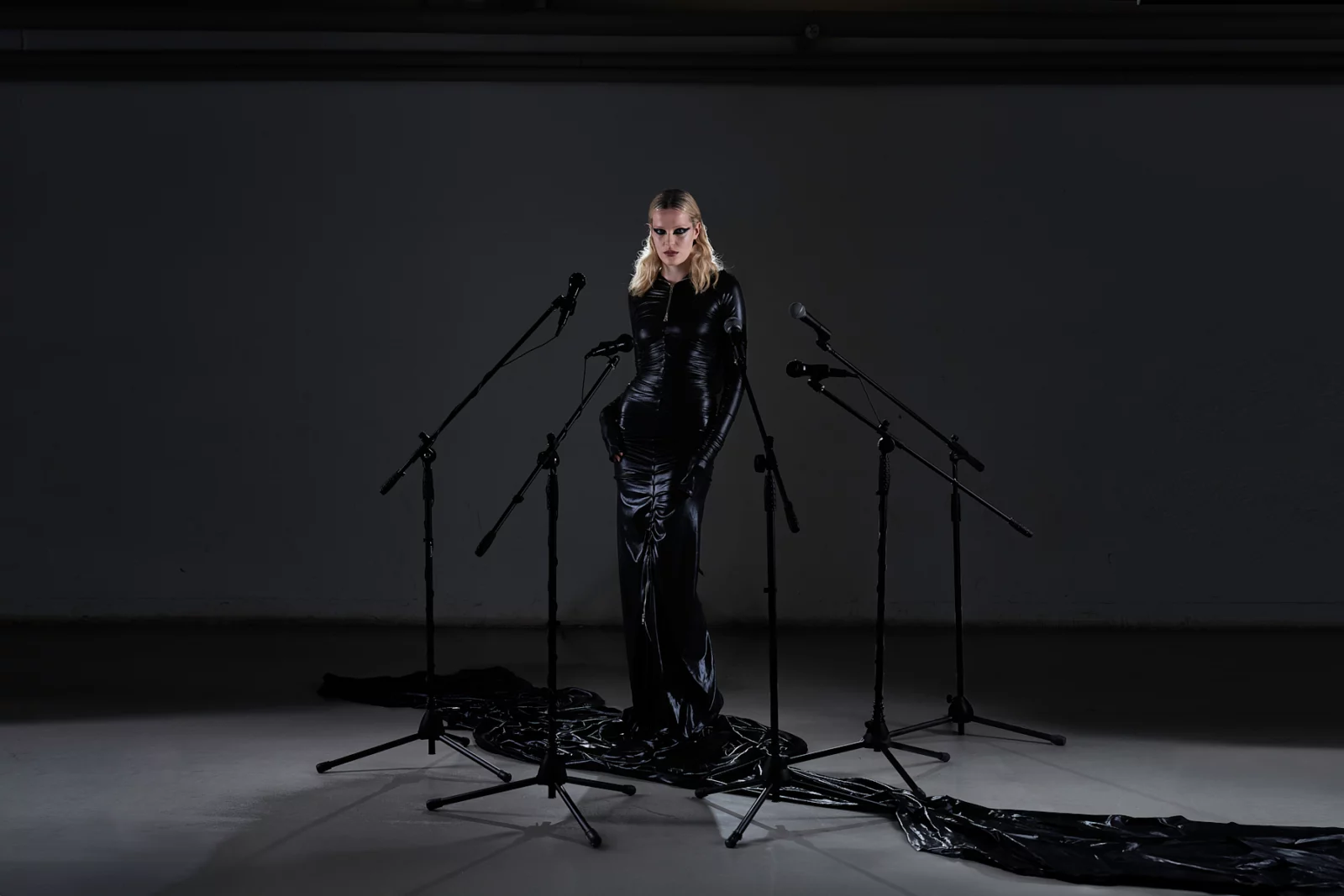 Full-length portrait of a blonde model in black performing between several microphone stands.