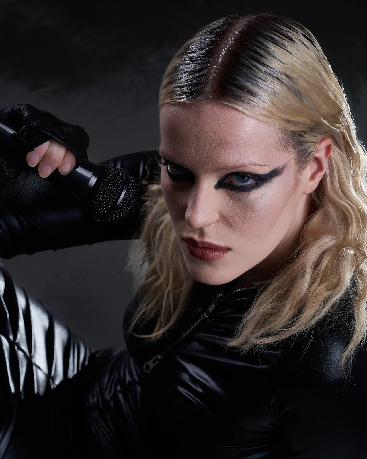 Close-up of a blonde model wearing dramatic winged eyeliner and glossy black clothing.