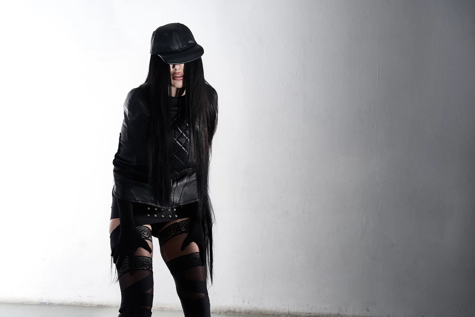 Full-length portrait of a model in a black hat, leather jacket and tall boots against white.