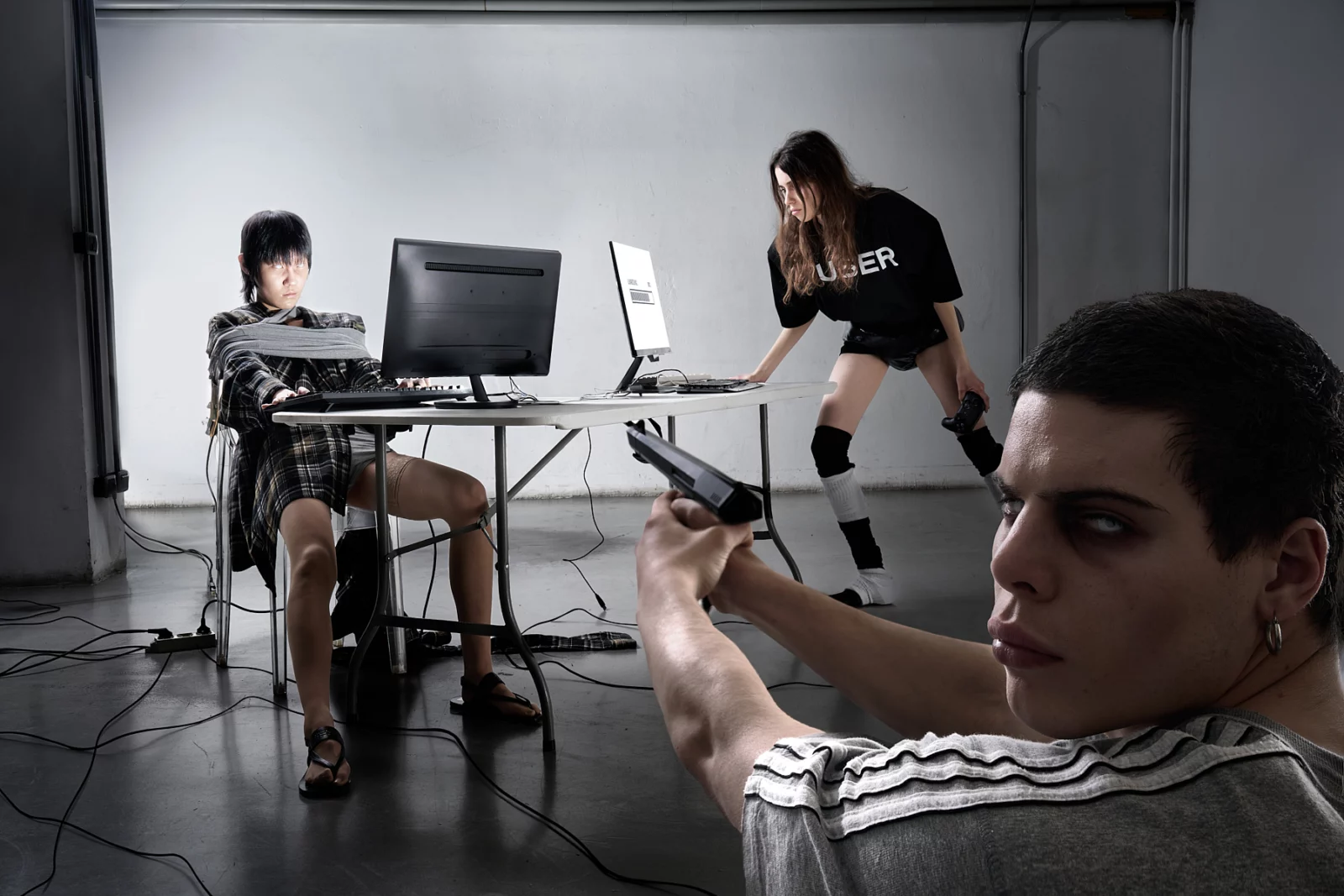 Two models working at computer monitors in a sparse studio setup, with another figure in the foreground.