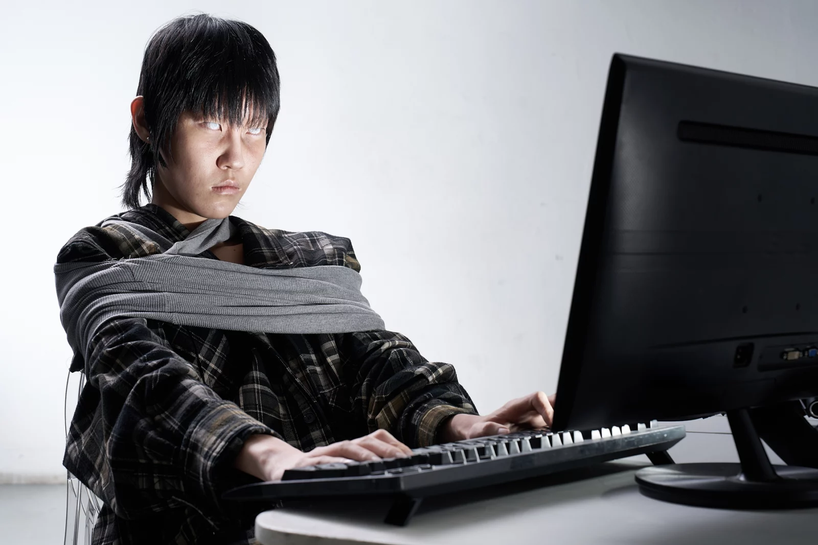Model wearing a wrapped gray top seated at a desk and typing on a keyboard.