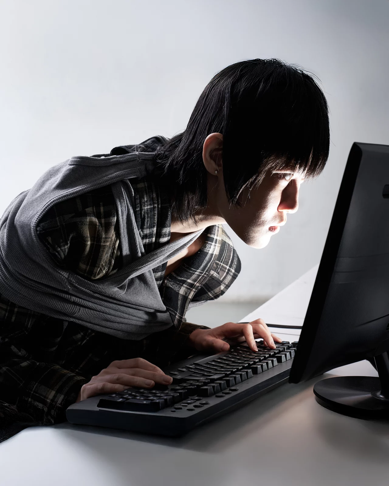 Profile of a dark-haired model leaning close to a computer keyboard and monitor.
