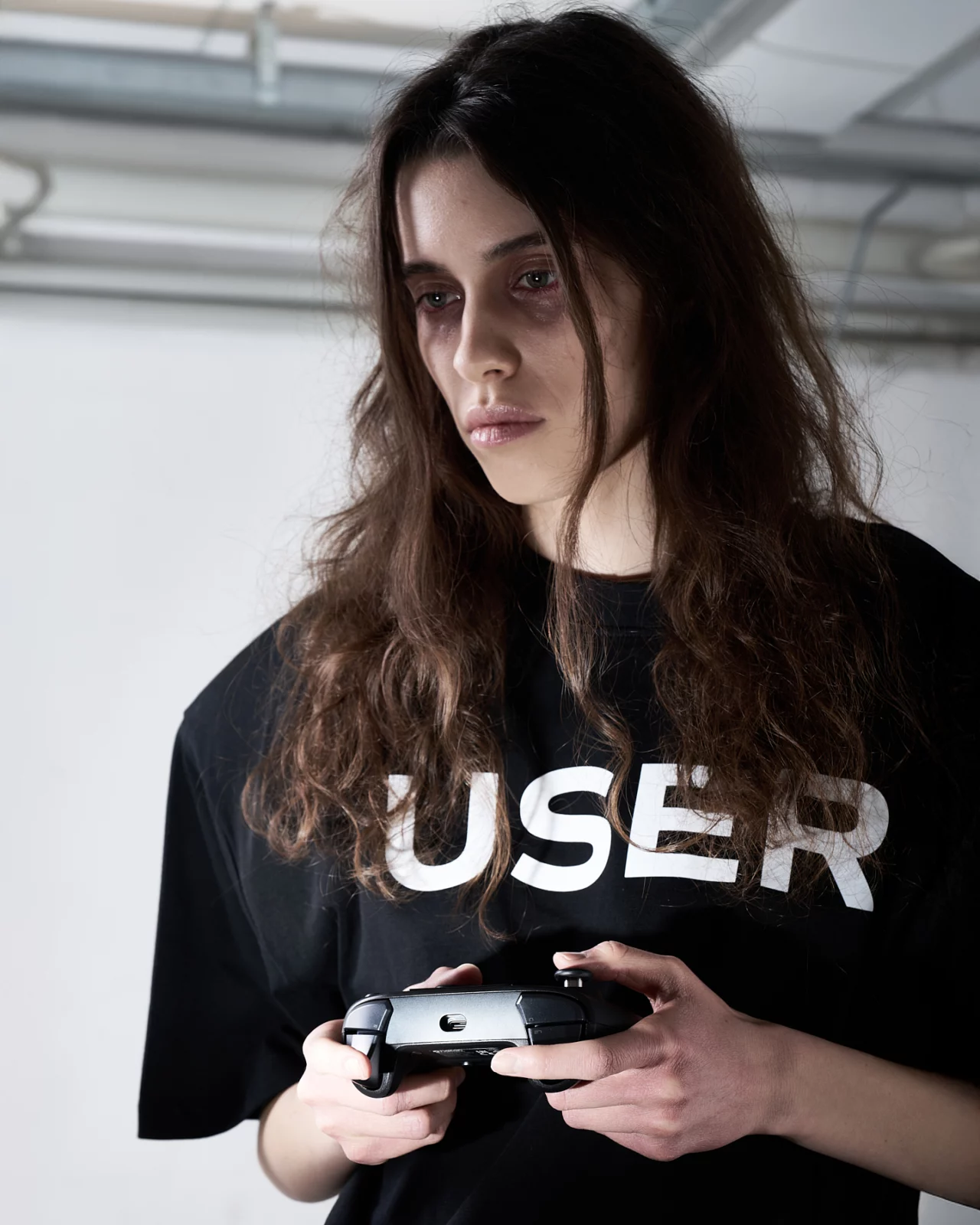 Portrait of a long-haired model wearing a black T-shirt with bold white lettering and holding a controller.