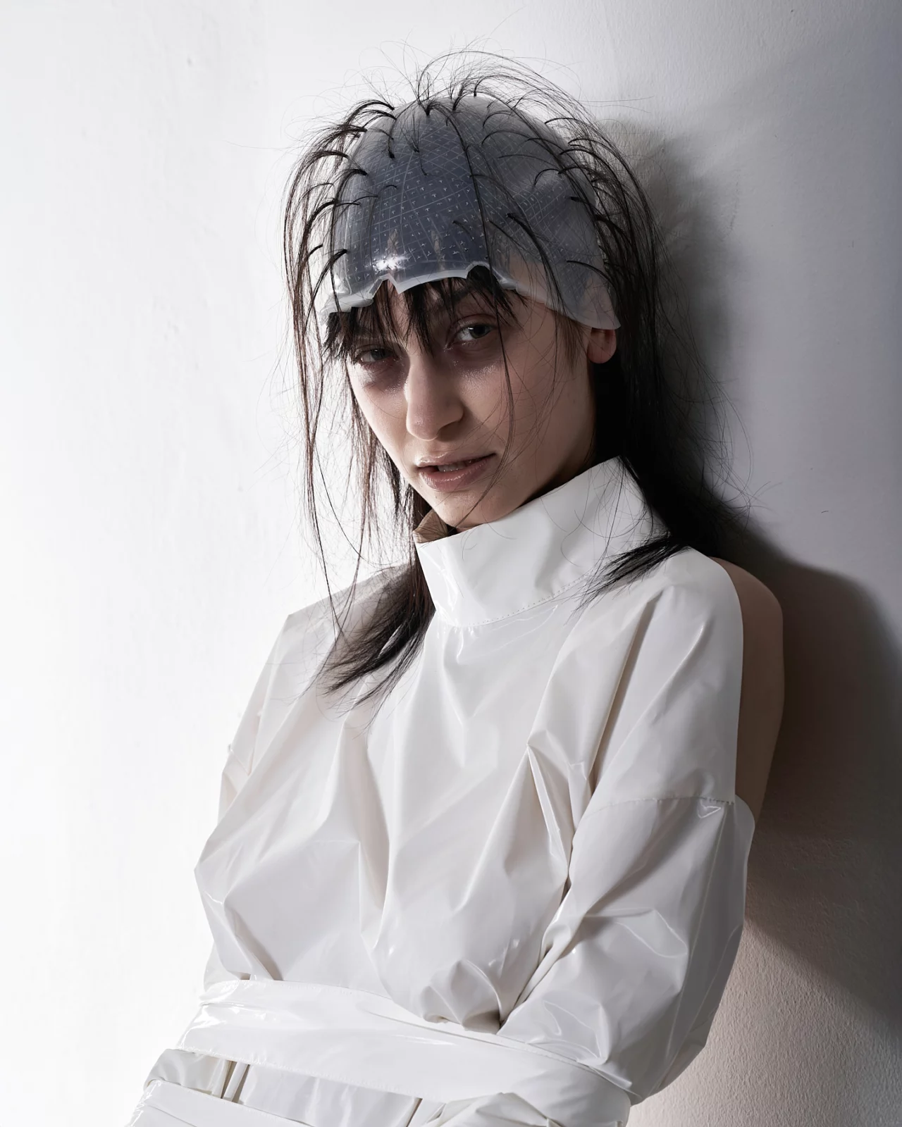 Portrait of a long-haired model in a structured white top and gauzy gray head covering.