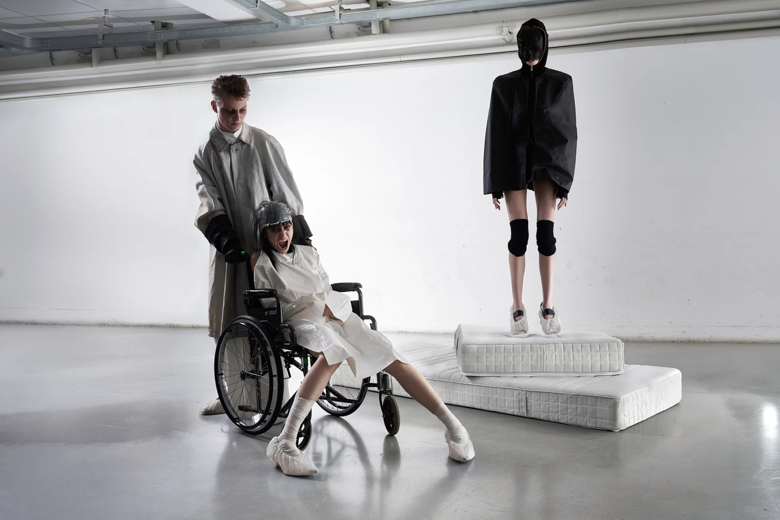 Wide studio scene with a model seated beside a mannequin-like figure on a raised white platform.
