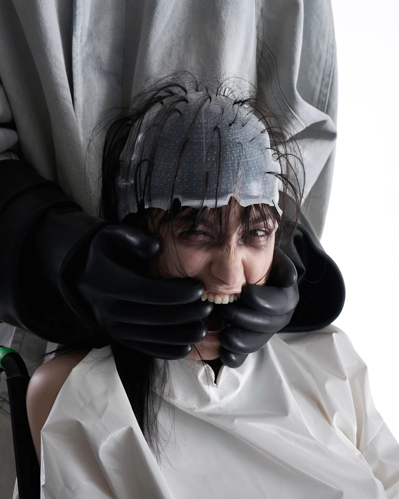 Fashion portrait of a model in a sculptural metallic headpiece and layered gray fabric covering the mouth.