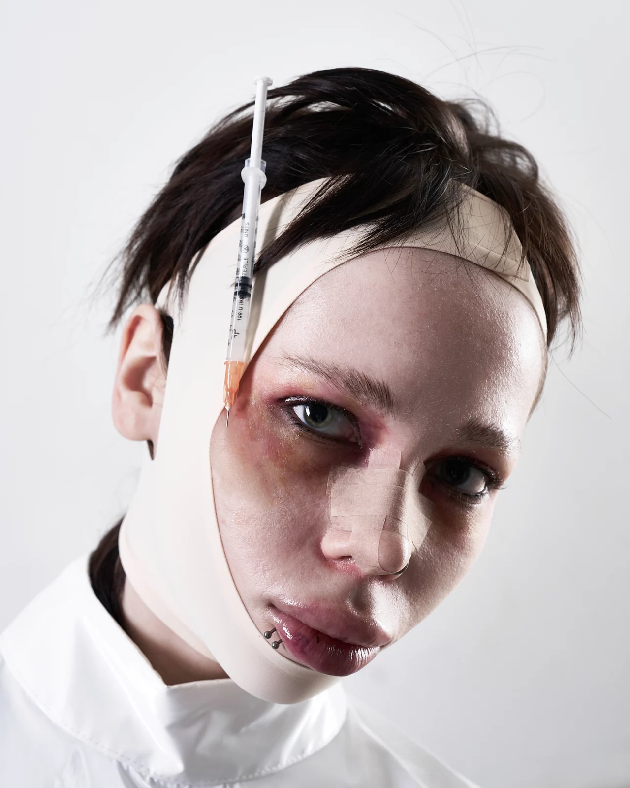 Tight beauty portrait of a short-haired model wearing a pale fabric head wrap and smoky eye makeup.