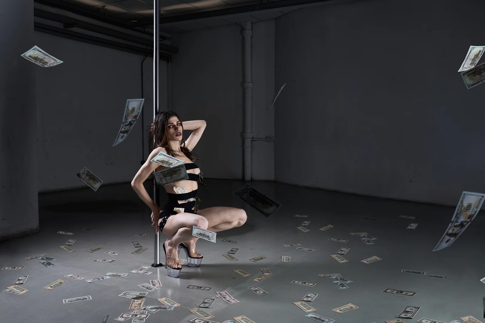 Model in a black-and-white cutout outfit posing on a chair in a dark studio with scattered papers.