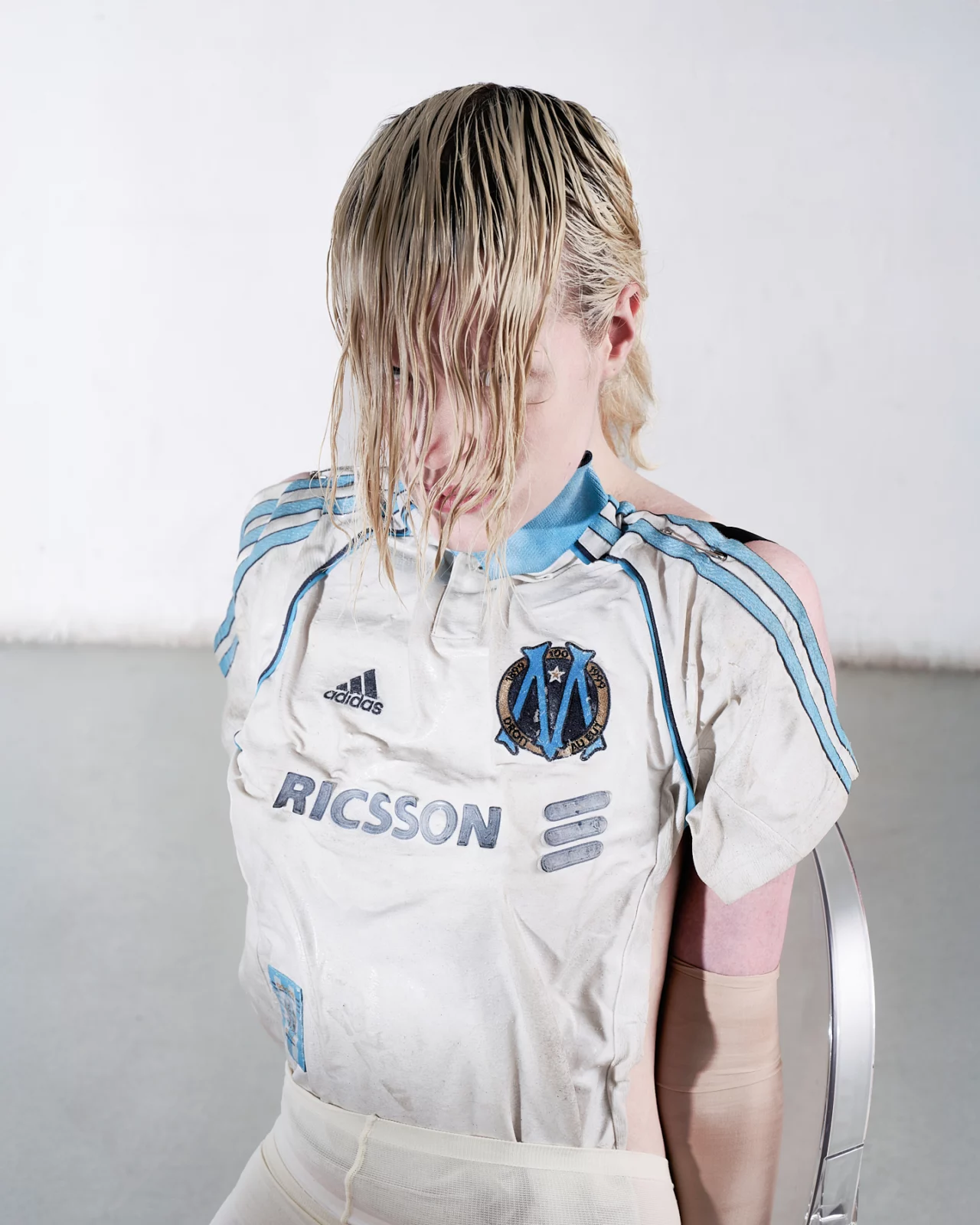Portrait of a blond model in a pale blue sports jersey with wet hair covering their face.
