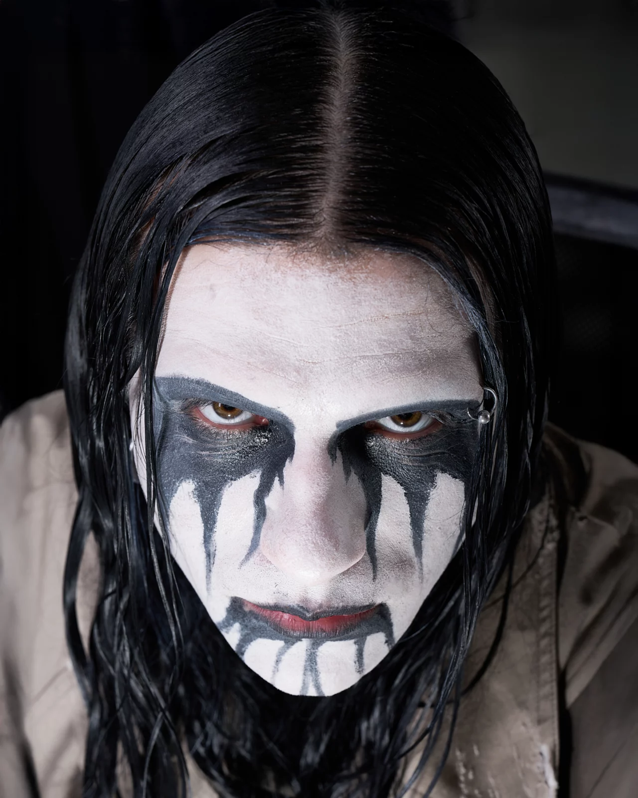 Intense close-up portrait of a long-haired model wearing black-and-white theatrical face paint.